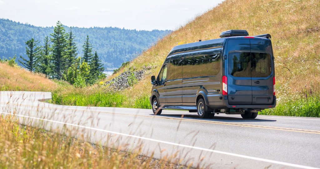 Small van driving on road between the hills